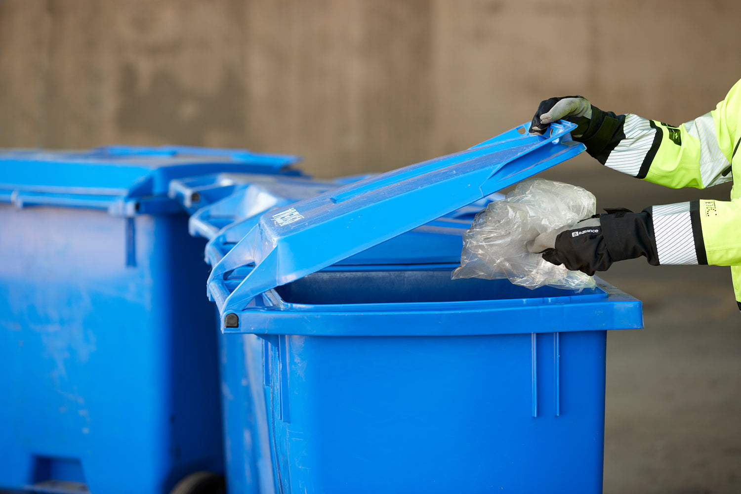Två händer som slänger plast i sopkärl i en återvinningscentral